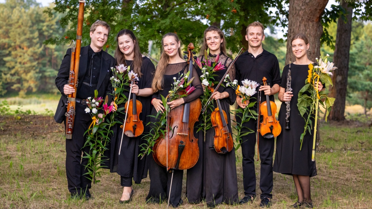 Seši jauni mūziķi melnās svinīgās drēbēs stāv ārā dabā, uz zāles fona ar kokiem. Viņi smaida un tur rokās savus mūzikas instrumentus un puķu pušķus. No kreisās puses redzams fagotists ar lilliju pušķi, divas vijolnieces ar vijolēm un ziediem, čelliste ar čellu un baltām lilijām, vijolnieks ar vijoli un baltu ziedu pušķi, kā arī obojiste ar oboju un saulespuķi