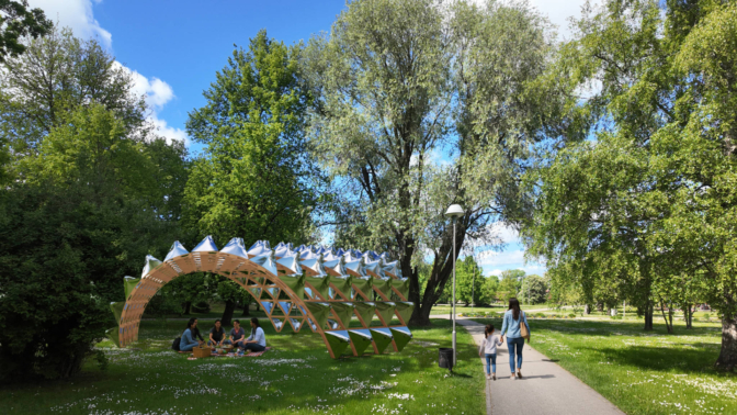 Saulainā parkā zem moderna, arkveida paviljona no koka un atstarojošiem paneļiem zālājā pikniko četras sievietes. Pa labi uz celiņa soļo māte ar bērnu, sadevušies rokās. Fona piepilda lieli zaļi koki un zilas debesis ar mākoņiem.